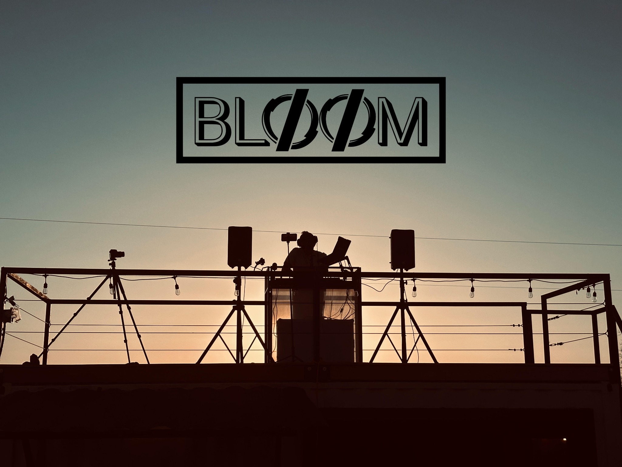 Brad Alba (DJ BLOOM) performing at sunset beneath the Bloom Event Collective logo